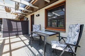 An outdoor patio with a table and two chairs, a large window, and a patterned floor. - Apartment 'Auszeit an der Eider' (Hennstedt)