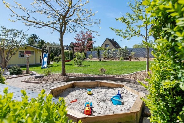 Un jardin avec un bac à sable, un toboggan et un petit abri de jardin.