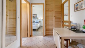 A room with a bed, wooden doors, a dining table with glasses and a bottle, and a wall with framed pictures. - Holiday Apartment Auszeit an der Eider – Relax in Idyllic Hennstedt (Hennstedt)