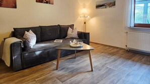 A living room with a dark brown sofa, a small coffee table, and three wall-mounted pictures. - Holiday Apartment Auszeit an der Eider – Relax in Idyllic Hennstedt (Hennstedt)