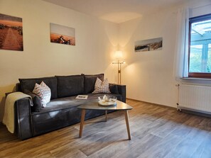 Un salon avec un canapé marron foncé, une petite table basse et trois tableaux accrochés au mur.