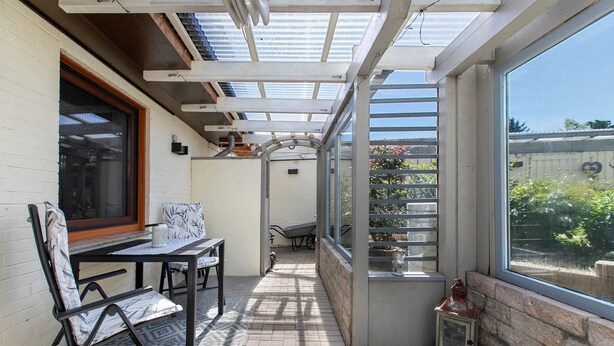 A covered patio with a table and chairs, a wheelbarrow, and a lantern. - Holiday Apartment Auszeit an der Eider – Relax in Idyllic Hennstedt (Hennstedt)