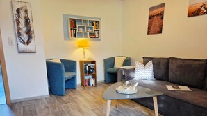 A living room with a sofa, two armchairs, a coffee table, a bookshelf, and a lamp. - Holiday Apartment Auszeit an der Eider – Relax in Idyllic Hennstedt (Hennstedt)