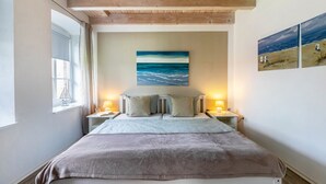 A bedroom with a bed, two bedside tables with lamps, a window, and a painting on the wall. - Apartment 'Ferienwohnung Hof Krakebüll' with Private Terrace, Private Garden and Wi-Fi (Humptrup)