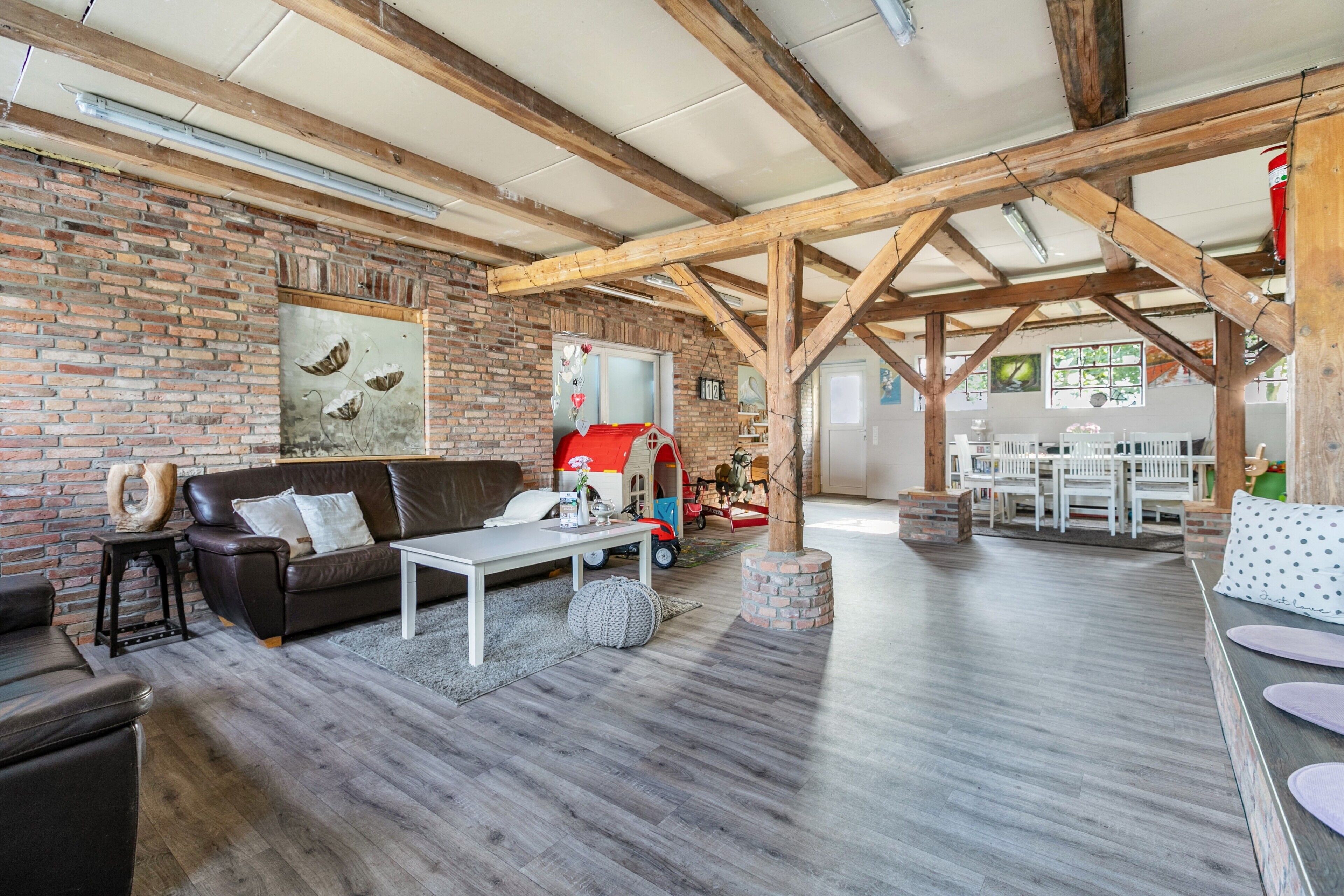 A spacious living area with a brick wall, wooden beams, a sofa, a coffee table, and a play area with a red toy car.