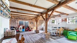 A spacious room with exposed wooden beams, a brick wall, a play area with toys, a dining table, and a green playpen. - Apartment 'Ferienwohnung Hof Krakebüll' with Private Terrace, Private Garden and Wi-Fi (Humptrup)