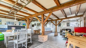 A spacious room with exposed wooden beams, a brick fireplace, and a dining area with white chairs and a table. - Apartment 'Ferienwohnung Hof Krakebüll' with Private Terrace, Private Garden and Wi-Fi (Humptrup)