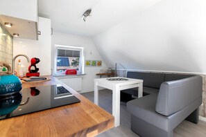 Une cuisine moderne avec un plan de travail en bois, une plaque de cuisson à induction noire, une table blanche et un canapé gris.