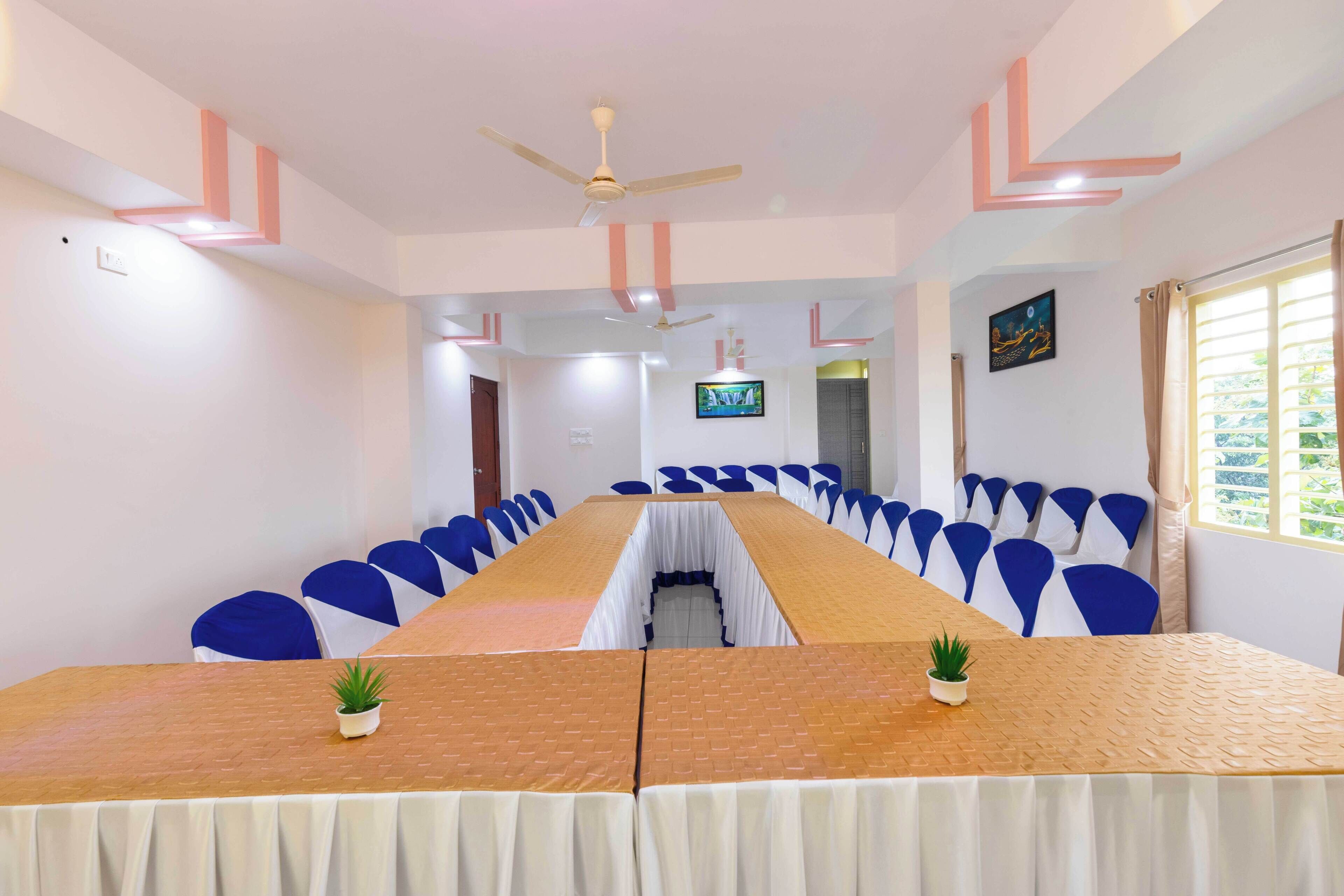 A conference room with a long table, blue chairs, ceiling fans, and a TV on the wall.