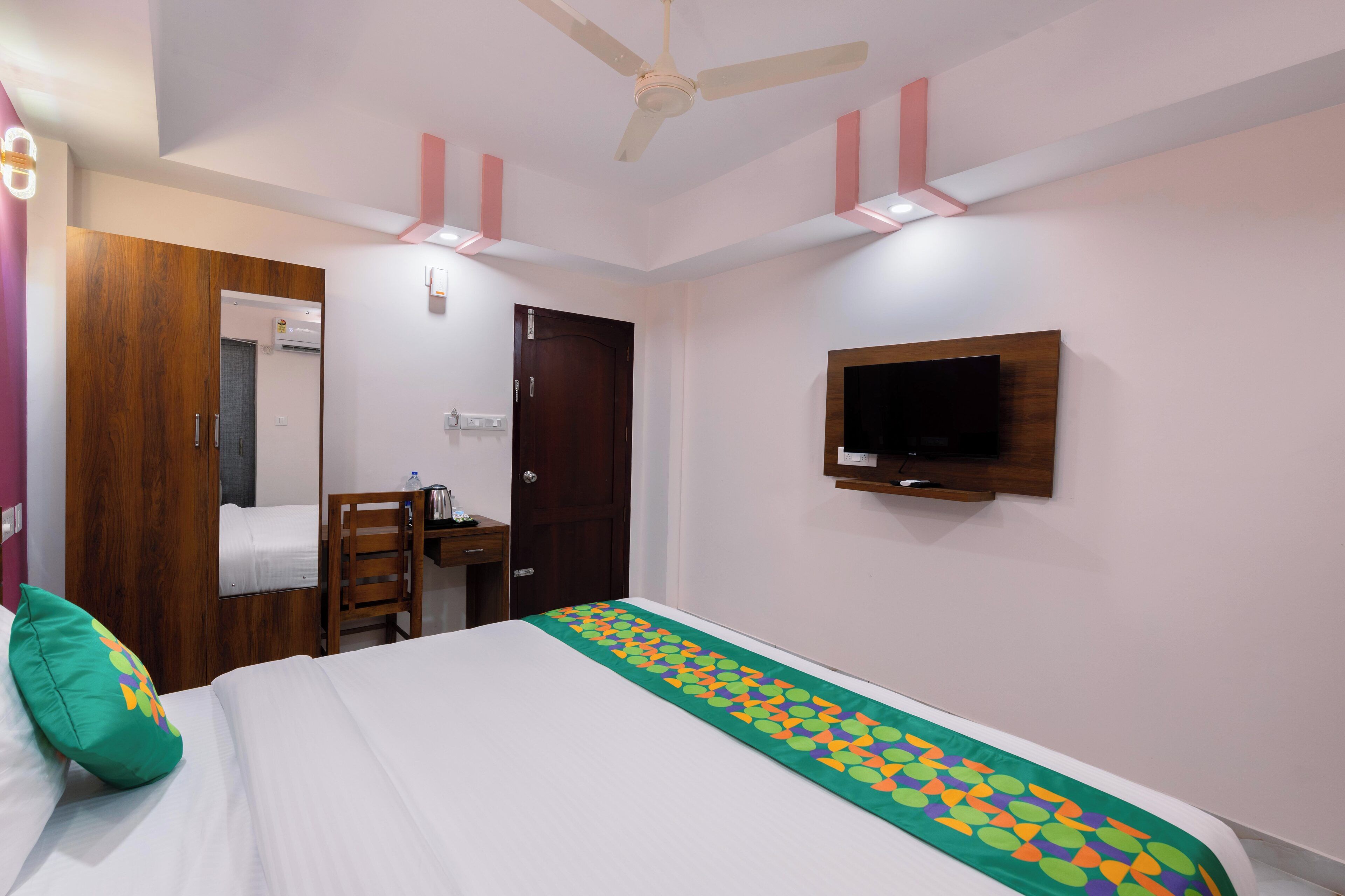 A hotel room with a bed, a desk, a chair, a TV mounted on the wall, and a ceiling fan.