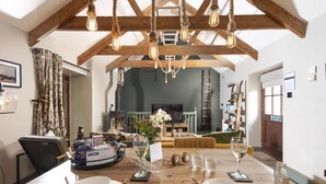 A dining area with a wooden table set for two, a fireplace in the background, and exposed wooden beams above. - Quaint and cosy, this reverse layout barn conversion exudes original charm and ultimate luxury. Quin (Camborne)