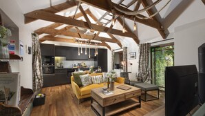A spacious living room with wooden beams, a yellow sofa, a wooden coffee table, and a television. - Quaint and cosy, this reverse layout barn conversion exudes original charm and ultimate luxury. Quin (Camborne)