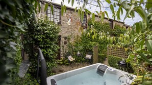 Un bain à remous dans un jardin, avec un mur en pierre et de la verdure.