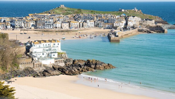 Une ville côtière dotée d’une plage de sable, d’une côte rocheuse et d’une structure fortifiée située au sommet d’une colline.