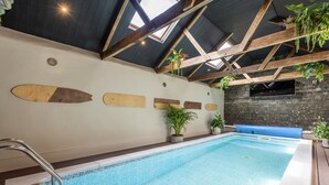Une piscine intérieure avec des poutres en bois, des plantes en pot et un mur en briques.