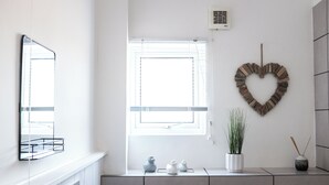 A bathroom with a white vanity, a heart-shaped wall decoration, a potted plant, and a small vase.