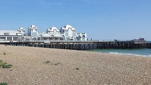 A coastal building with a pier extending into the sea, surrounded by a pebbled beach.