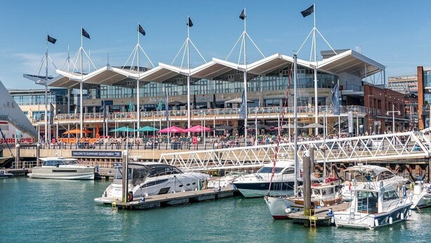 A marina with boats docked, a modern building with multiple floors, and a bridge connecting different areas.