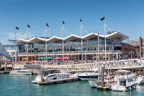 Una marina con barcos amarrados, un edificio moderno de varios pisos y un puente que conecta diferentes zonas.
