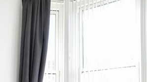 A modern room with a grey upholstered armchair, a small round table with a vase, and a window with white blinds.