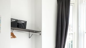 A modern bedroom with a bed, a chair, a shelf with baskets, and a window with curtains.
