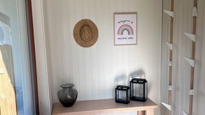 Een gang met een houten bankje, een aan de muur bevestigde hoed, een bord met een welkomstboodschap en een vaas.