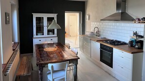 Een moderne keuken met een houten eettafel, witte kasten en een zwarte achterwand.