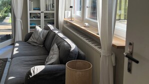 Een gezellige woonkamer met een grijze bank, een boekenkast en een raam met gordijnen.