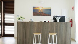 A reception desk with a painting of a lighthouse, two white stools, a fire extinguisher, and a coffee machine. - Masseria Pozzelle (Giurdignano)