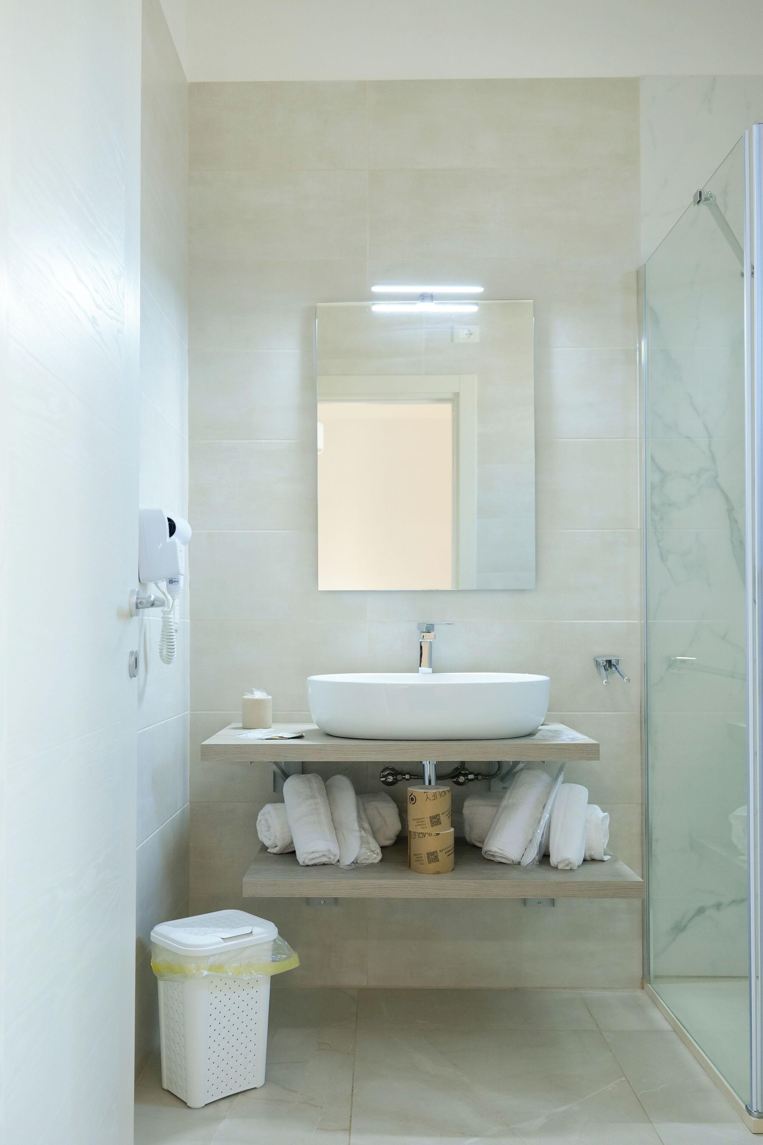 Un baño moderno con un espejo grande, un lavabo blanco y una cabina de ducha de vidrio.