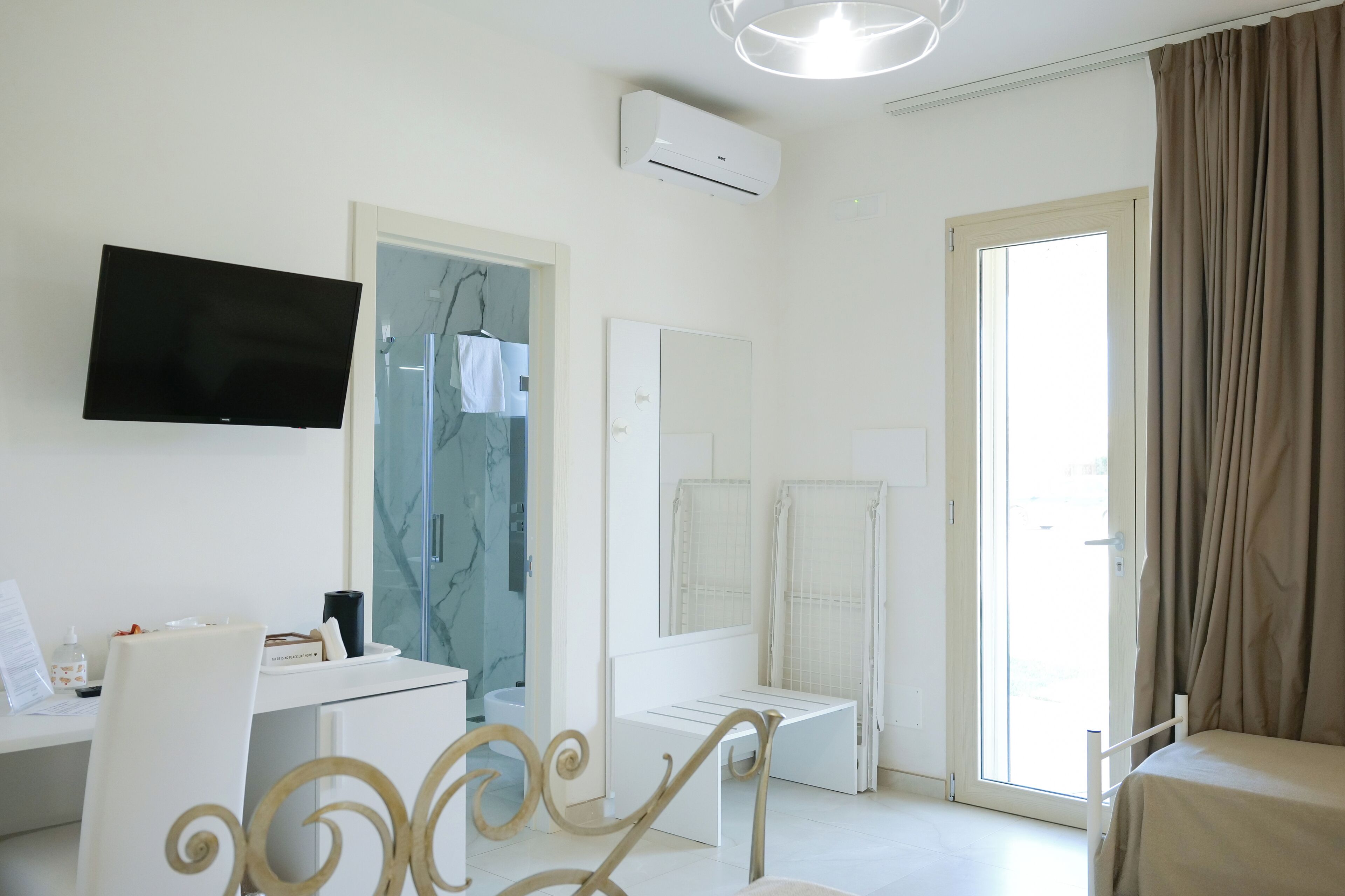 Une chambre d’hôtel équipée d’un téléviseur à écran plat, d’un bureau avec des articles de toilette, d’une douche avec une porte en verre, d’un lit avec une tête de lit et d’une grande fenêtre avec des rideaux.