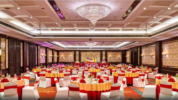 Uma sala de banquetes com mesas redondas, cadeiras brancas e fitas vermelhas.