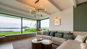 A modern living room with a large window, a sofa, two round coffee tables, and a unique ceiling light fixture. - Attractive villa with jetty (Kamperland)