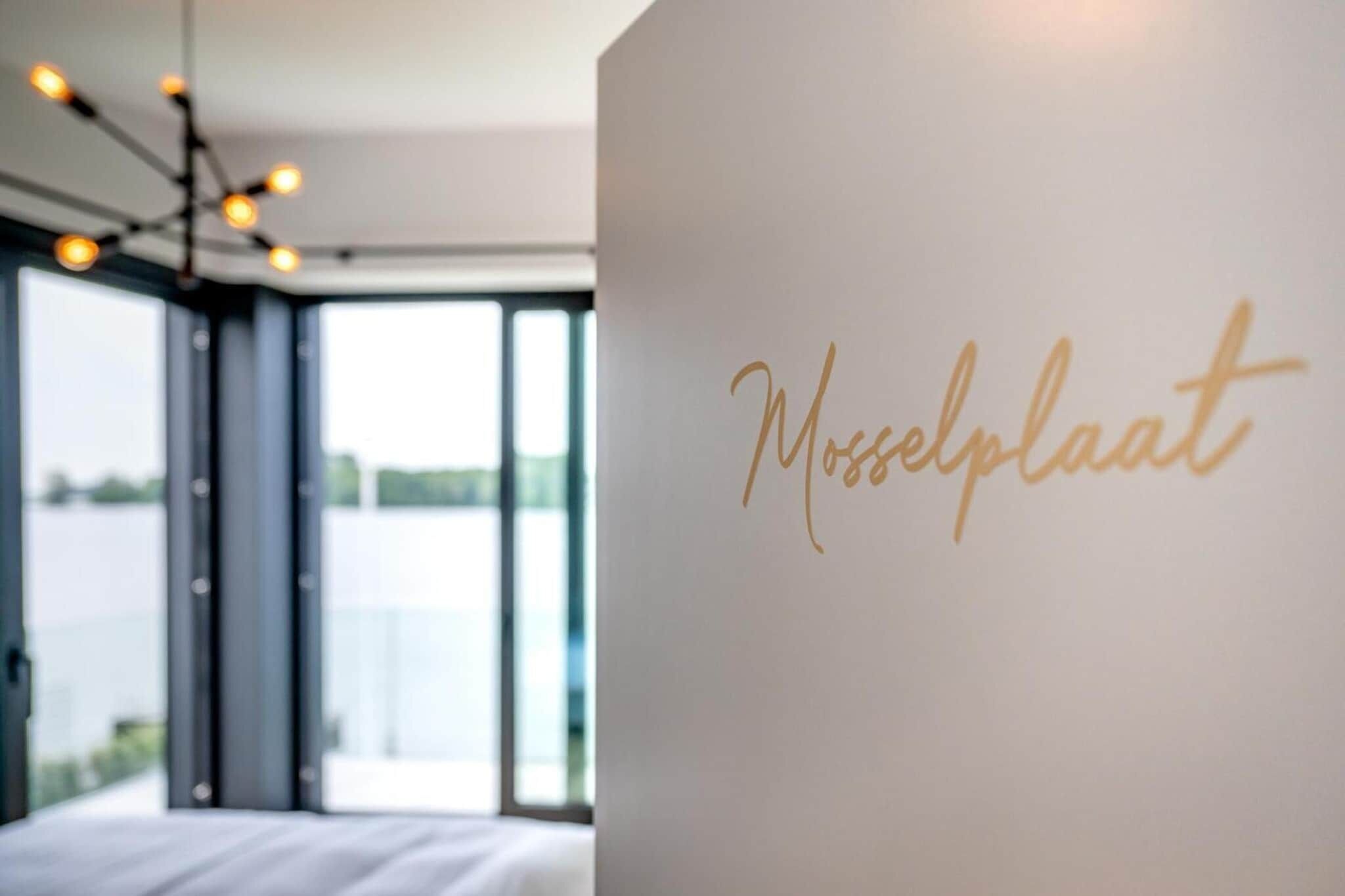 Een kamer met een groot raam, een bed en een muur met de tekst 'Mosselplaat' in goud.