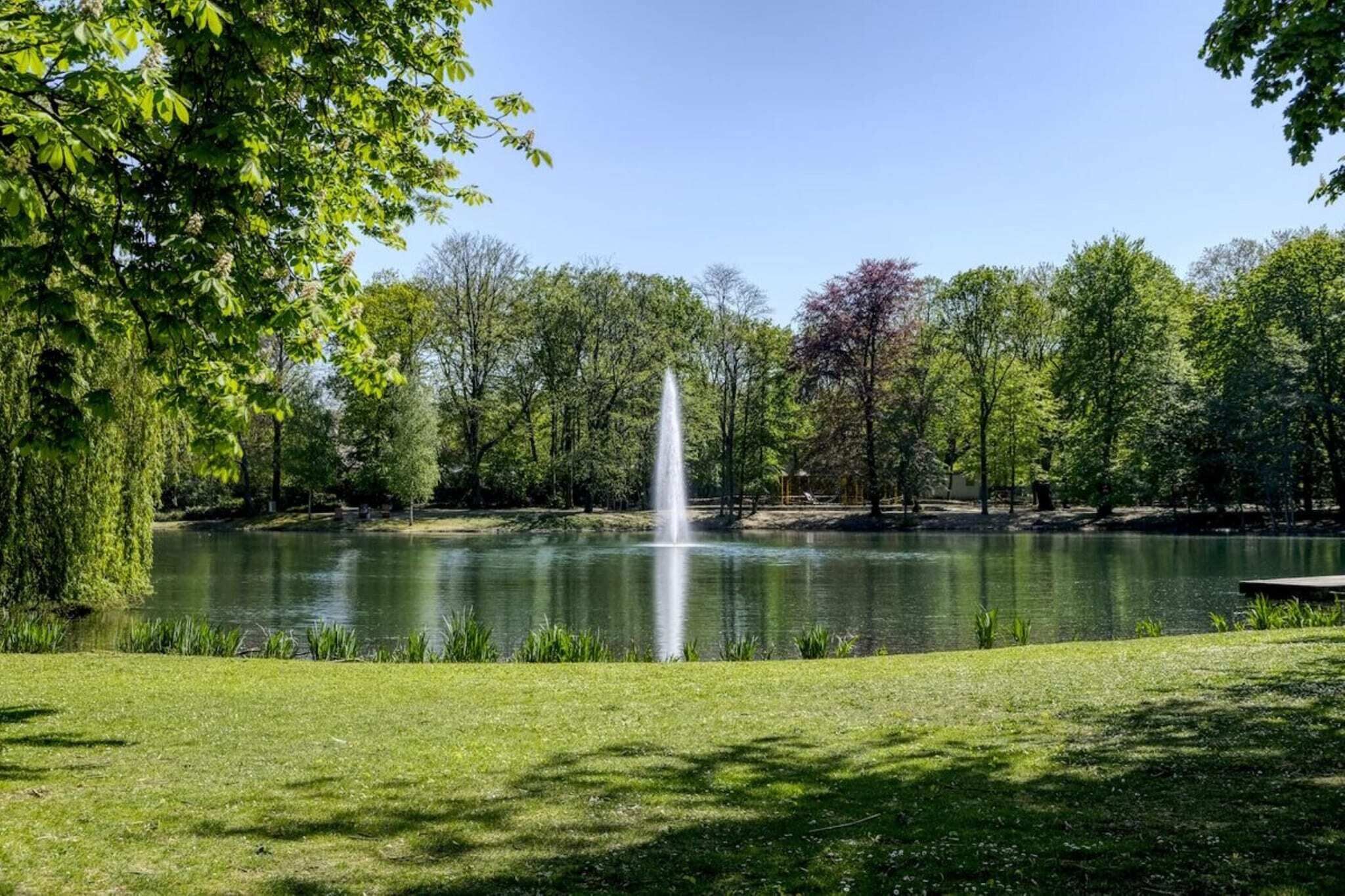 Un parc paisible avec une fontaine, une végétation luxuriante et un ciel dégagé.