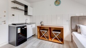 A compact kitchen with a dishwasher, a coffee maker, and a wooden bench with metal shelves.