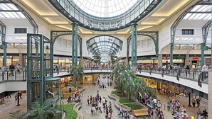 A multi-level shopping mall with a central atrium, escalators, and various retail stores.