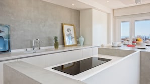 A modern kitchen with a central island, a built-in oven, and a large window offering a view of the city. - Solaga - Linaje (Málaga)