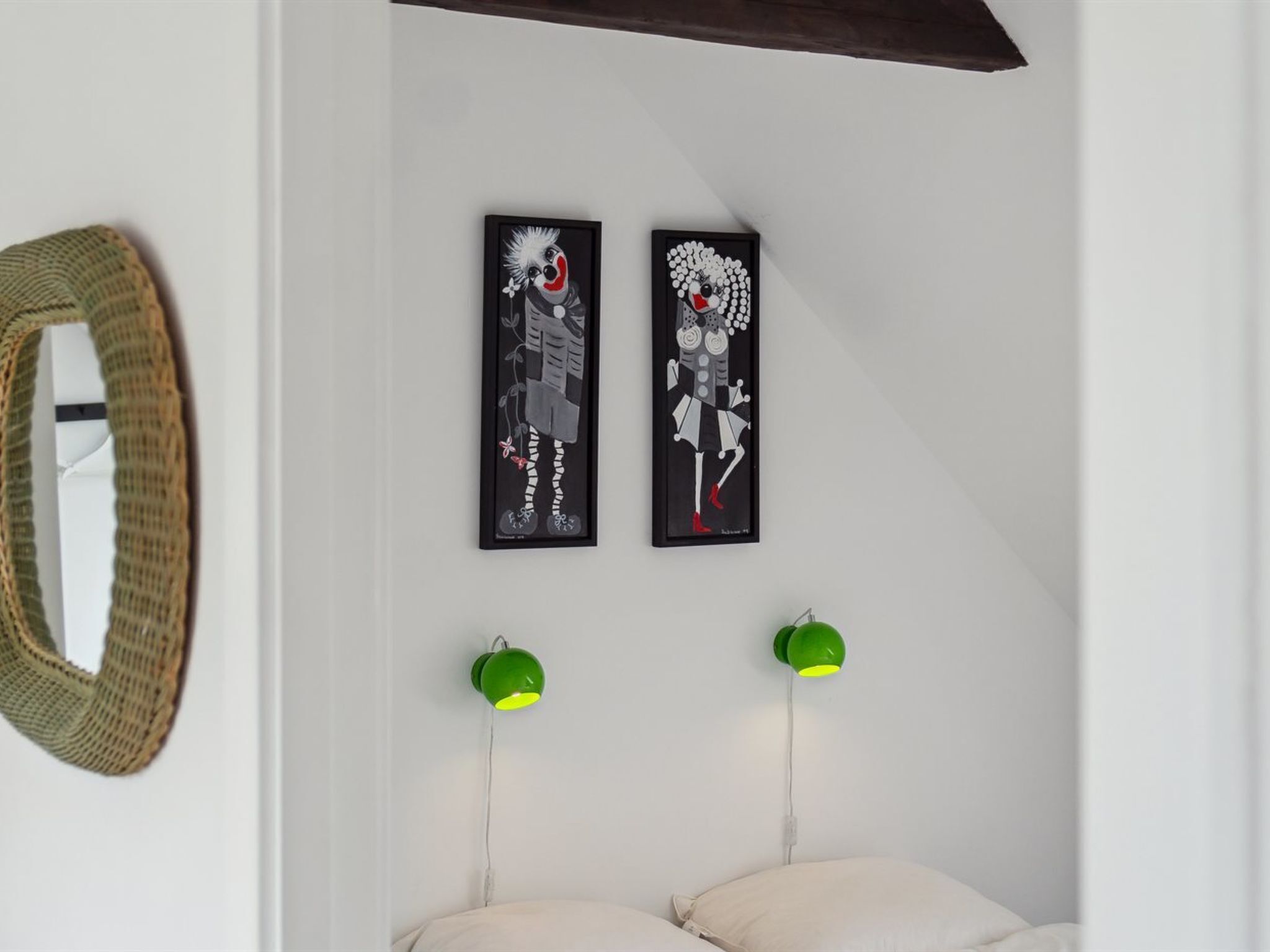Ein Schlafzimmer mit zwei gerahmten Kunstwerken, einem gewobenen Korb und zwei grünen Wandlampen.