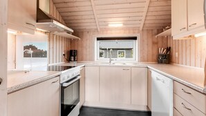 Ett kompakt kök med träskåp, en inbyggd ugn, en kaffebryggare och ett fönster med utsikt över omgivningen.