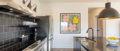 Una cocina moderna con encimera negra, electrodomésticos de acero inoxidable y una lámpara colgante negra.