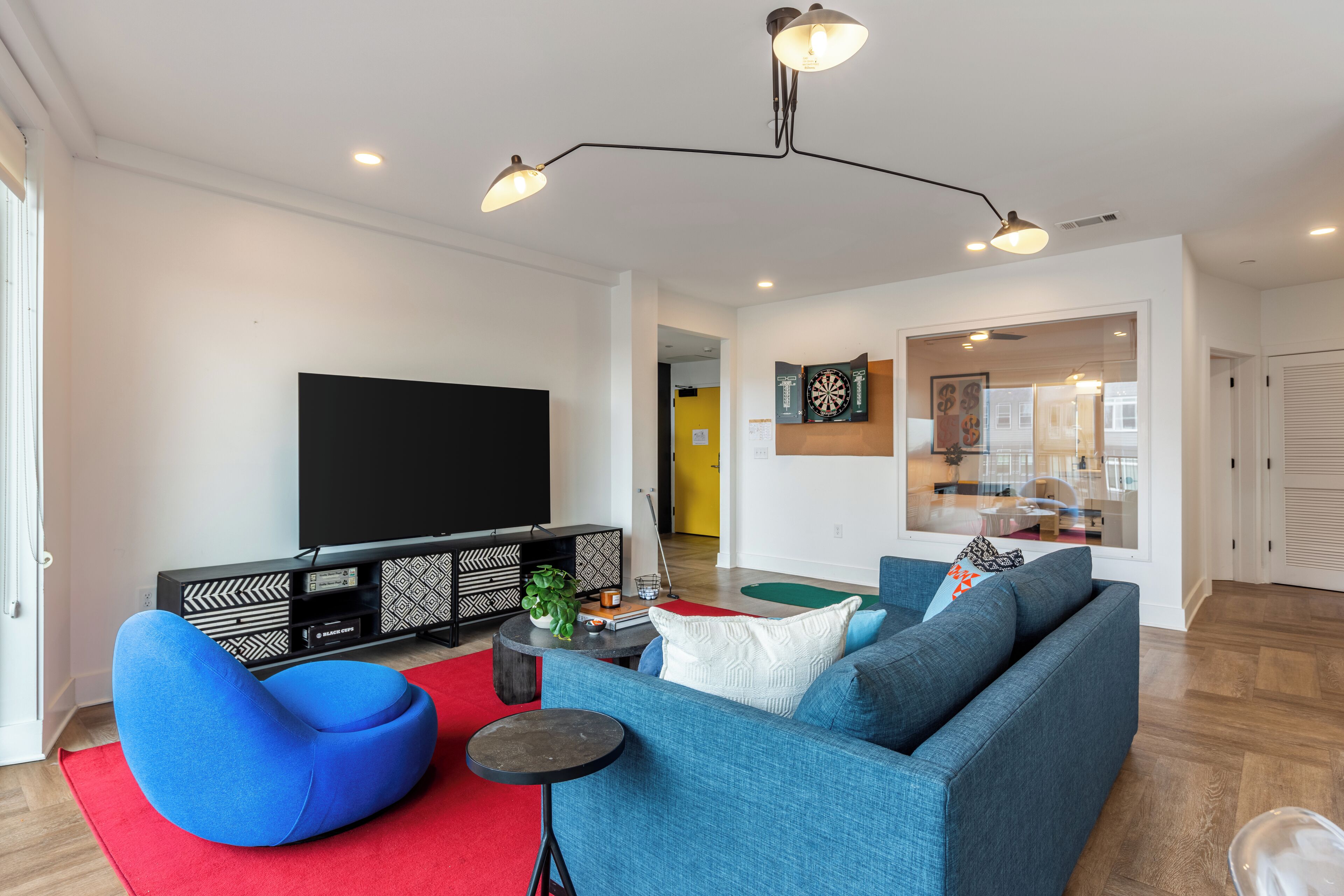 Una sala de estar moderna con un sofá azul, un tapete rojo, un mueble de entretenimiento negro y un televisor de pantalla plana.