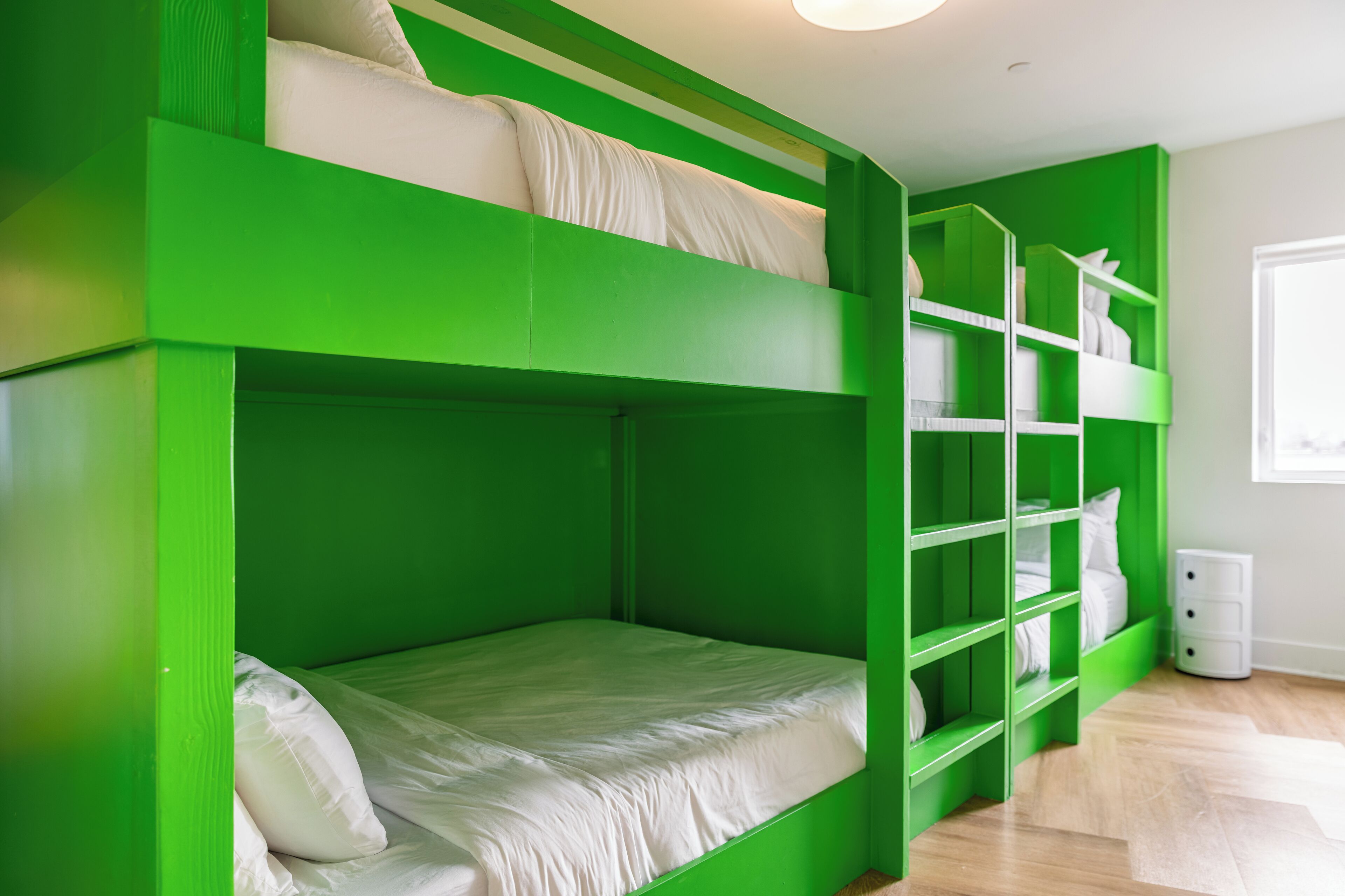 Habitación con literas, paredes verdes y ropa de cama blanca.