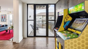A modern living room with a red carpet, a blue sofa, and a coffee table. There is a large window with a view of a balcony and a building. - Bachelor Party Pad, 5 Minutes to Broadway + Private Balcony | Last Call (Nashville)