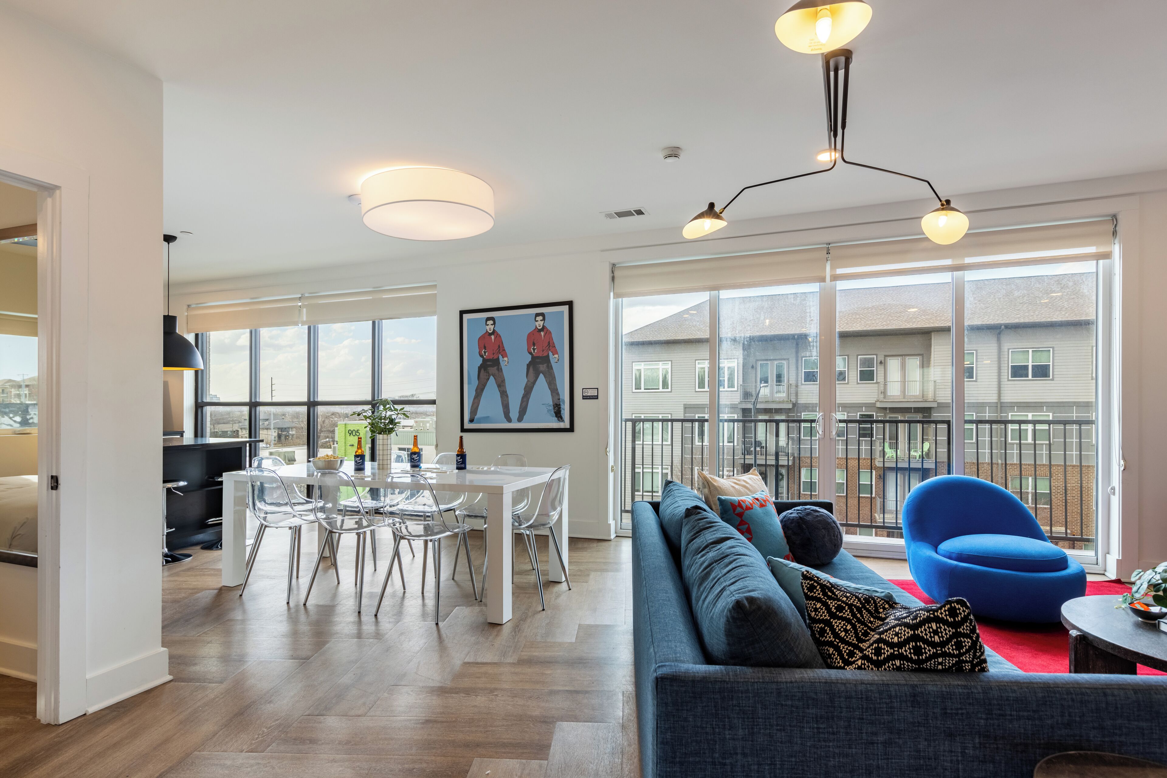 Un moderno salón con un sofá azul, una mesa de comedor con sillas y grandes ventanales que ofrecen vistas a la ciudad.