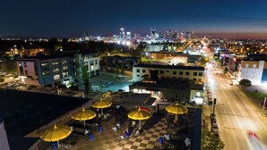 A rooftop terrace with outdoor seating and umbrellas, overlooking a cityscape with buildings and a skyline.