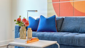 A modern living room with a blue sofa, decorative pillows, a white coffee table, and a vase with flowers.