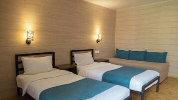 A hotel room with two single beds and a sofa bed, wooden panel walls, and wall-mounted lighting.