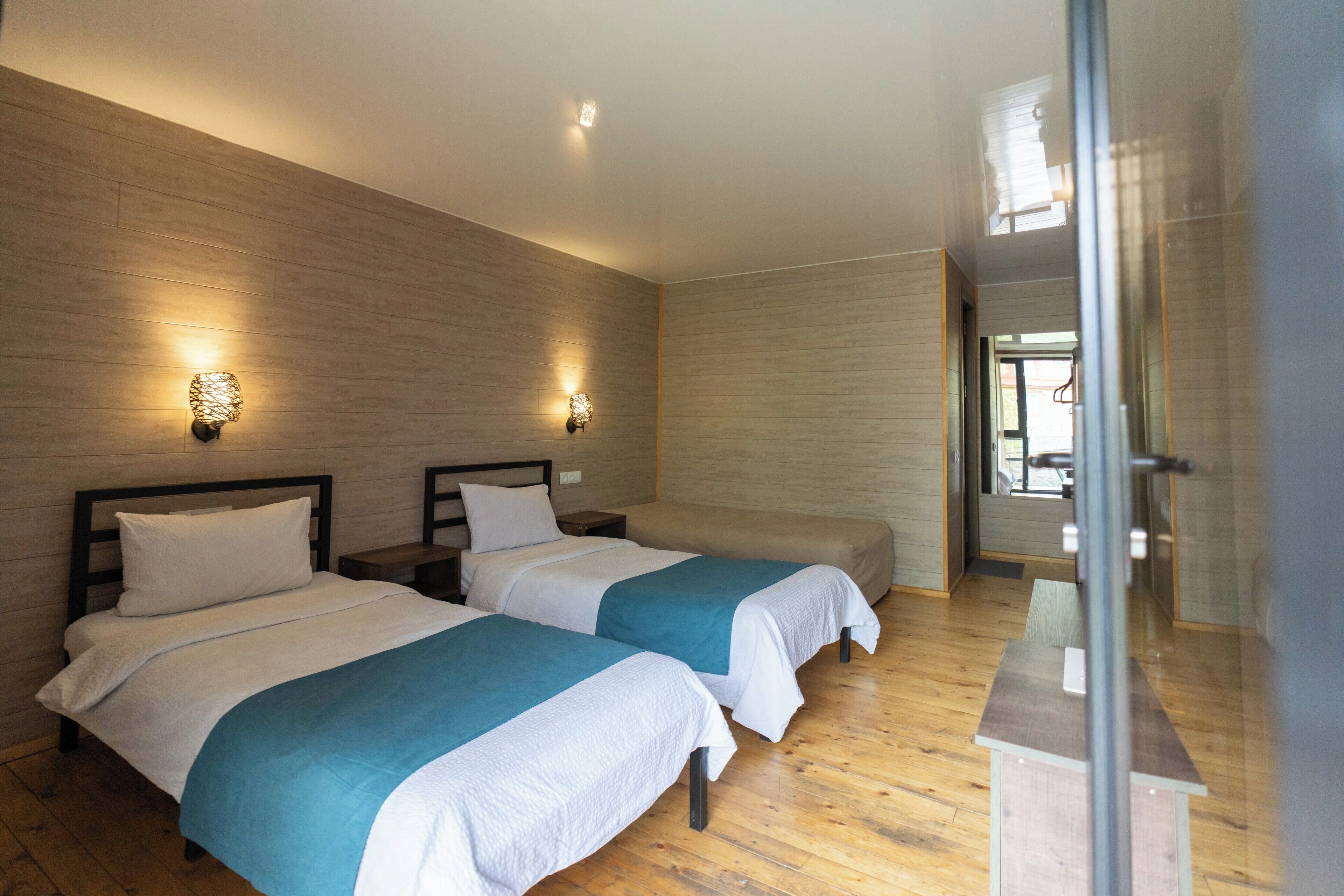 Een hotelkamer met twee bedden, houten vloer en wandlampen.