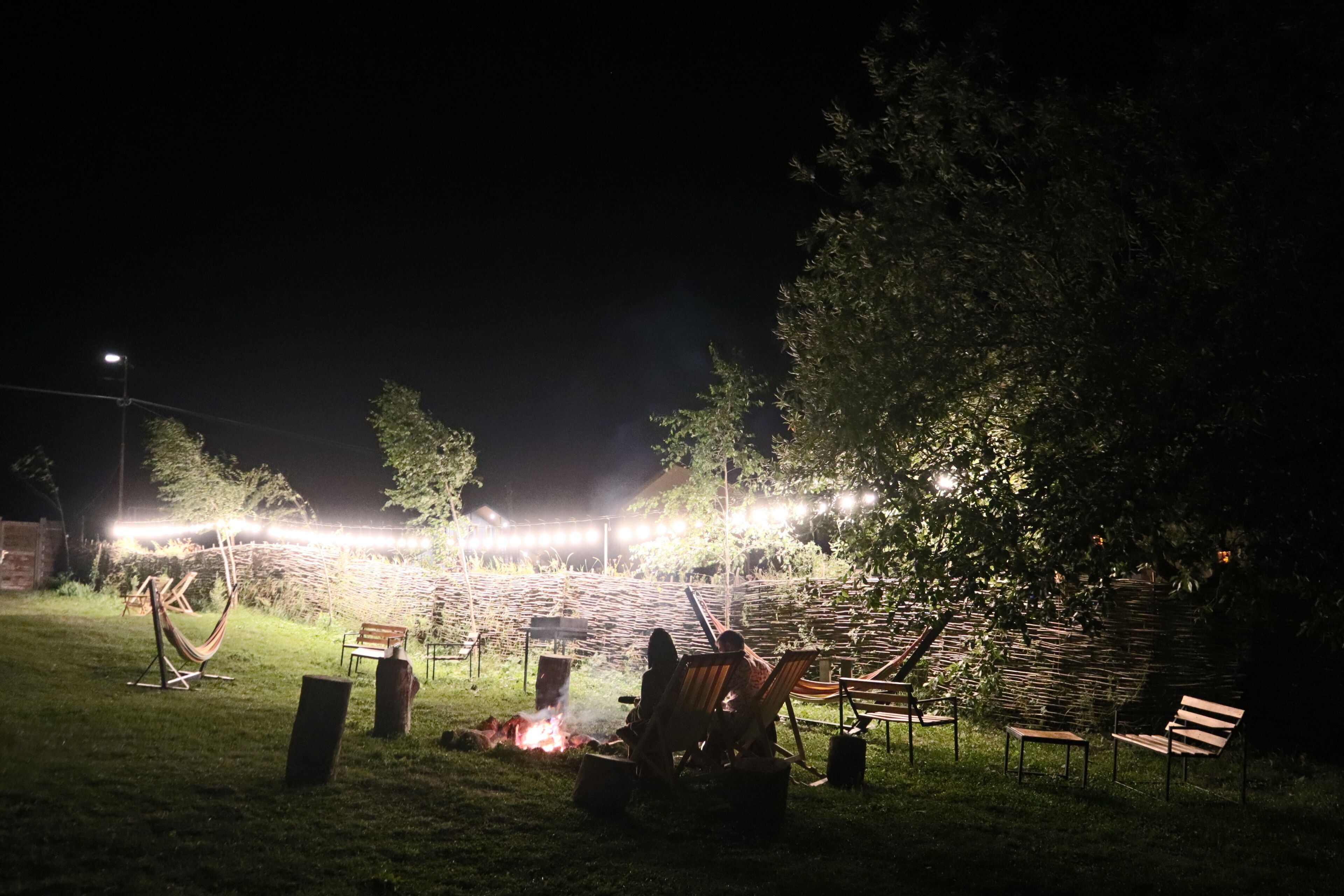 Un espacio al aire libre con asientos nocturnos, una chimenea, sillas y luces colgantes.